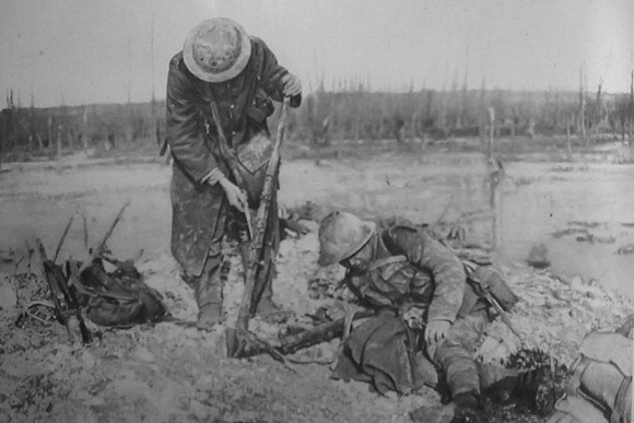 A Mud Splattered Soldier Picking Out The Mud From His Rifle