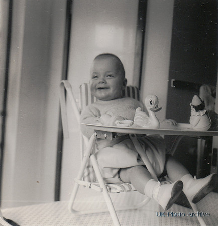 A Baby In A Highchair With Toy Duck And Clown c.1950s